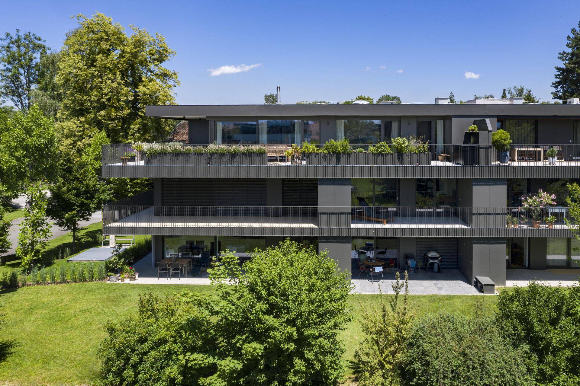 Vorderansicht des modernen Gebäudes mit großzügigen Balkonen und Terrassen sowie Gartenbereich.