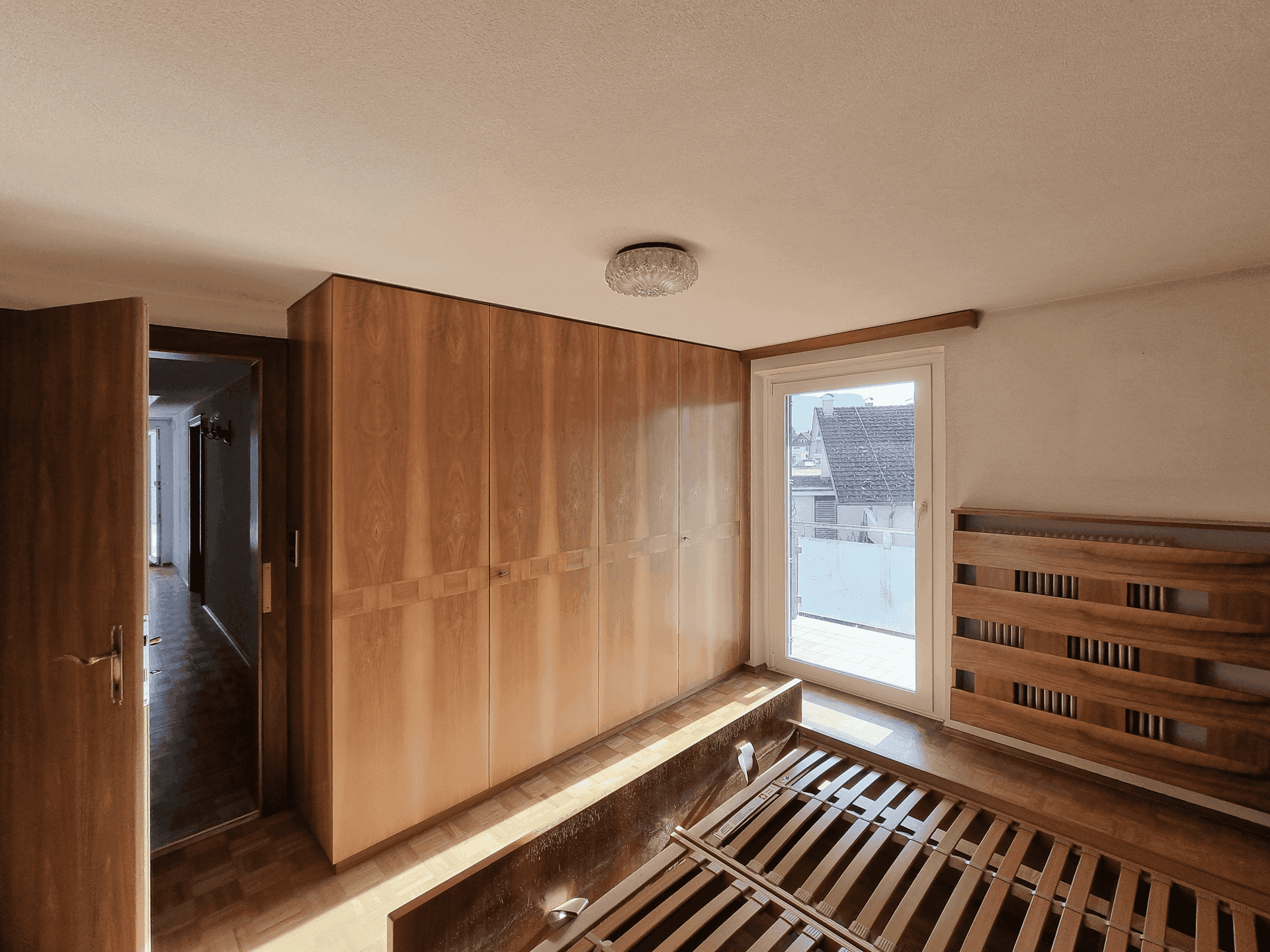 Schlafzimmer mit Einbauschränken aus Holz und Zugang zu einem kleinen Balkon.