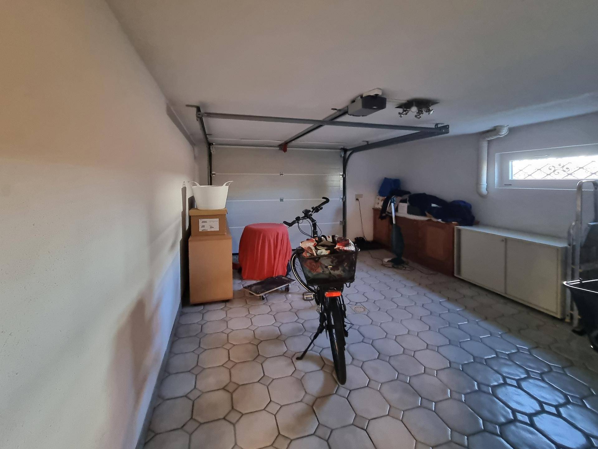 Garage mit Fliesenboden, Platz für Fahrräder und Stauraum.