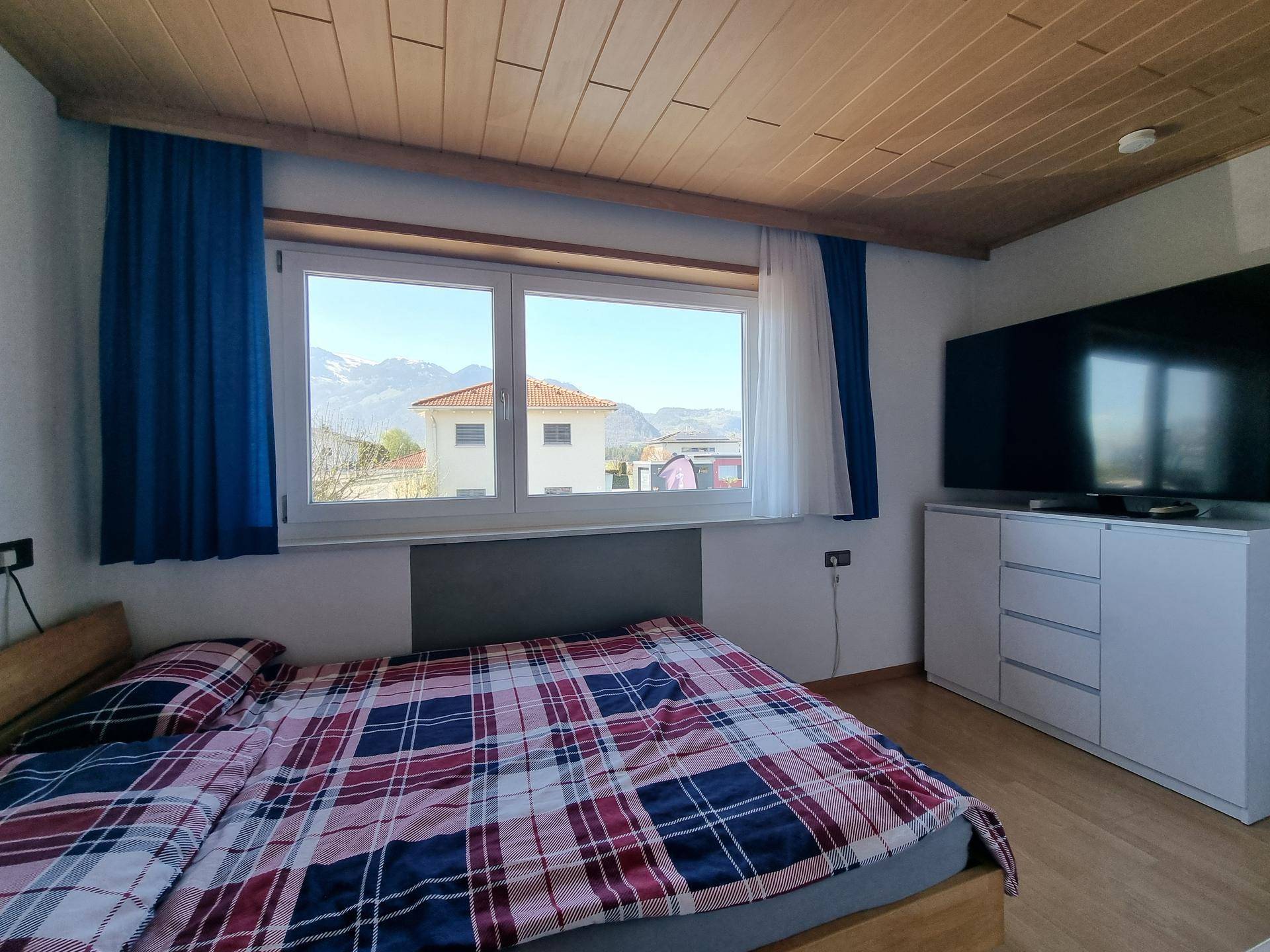 Schlafzimmer mit Holzdecke, großem Fenster und Bergblick.