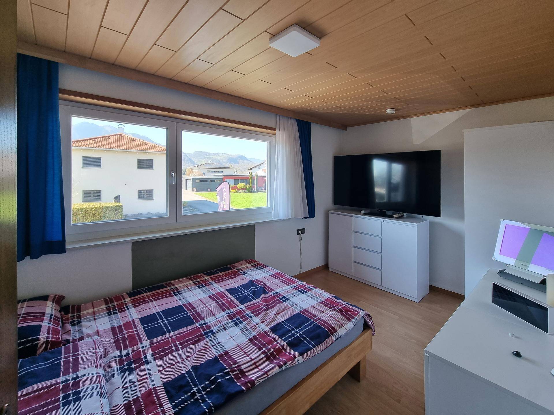 Helles Schlafzimmer mit Holzdecke, Fernseher und Ausblick auf die Umgebung.
