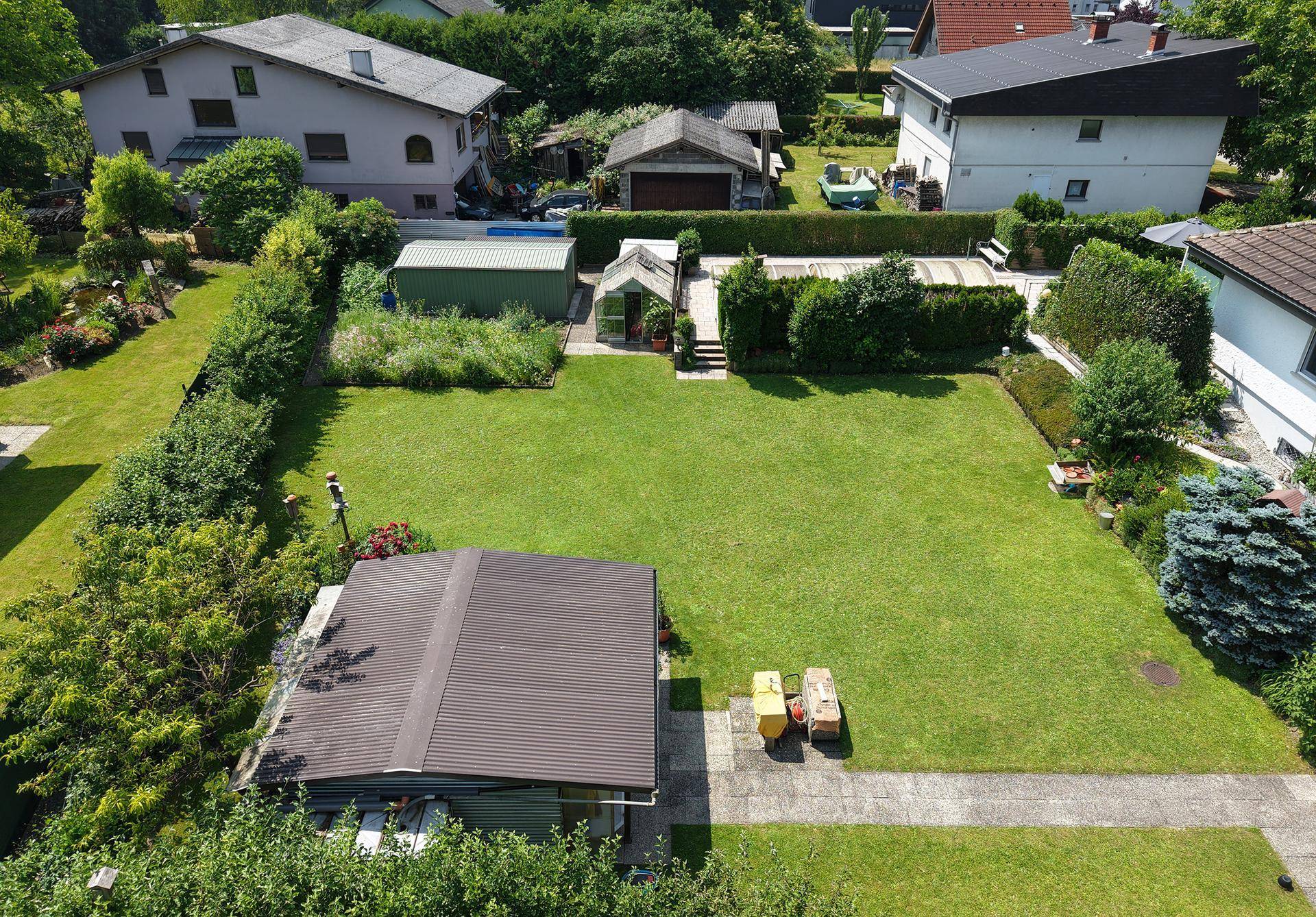 Großer, gepflegter Garten mit Rasenfläche, Hecken, Gartenhaus und Gewächshaus.