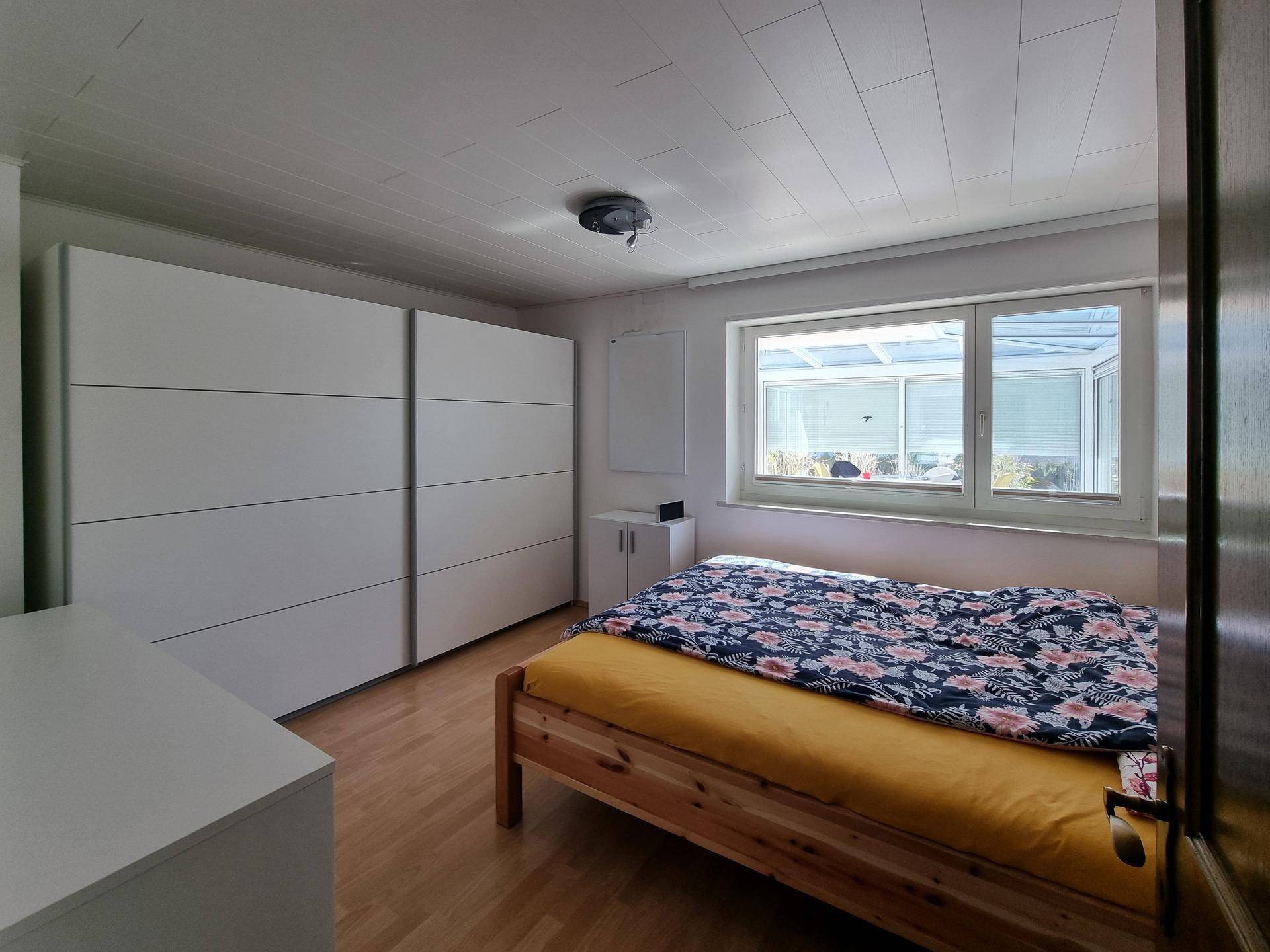 Schlafzimmer mit großem weißen Kleiderschrank und Blick in den Wintergarten.