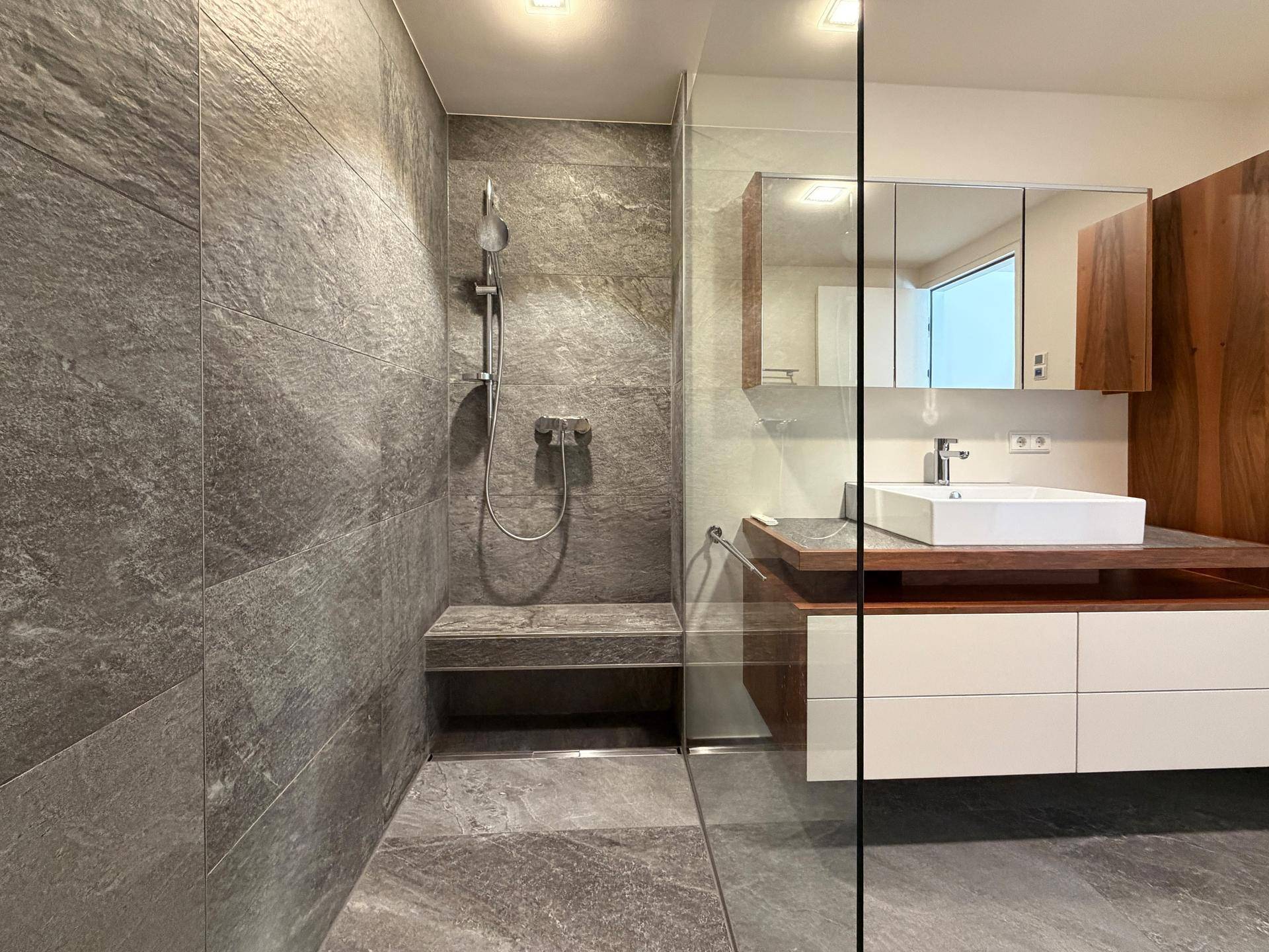 Geräumige begehbare Dusche mit Sitzbank und modernem Waschtisch im Badezimmer.