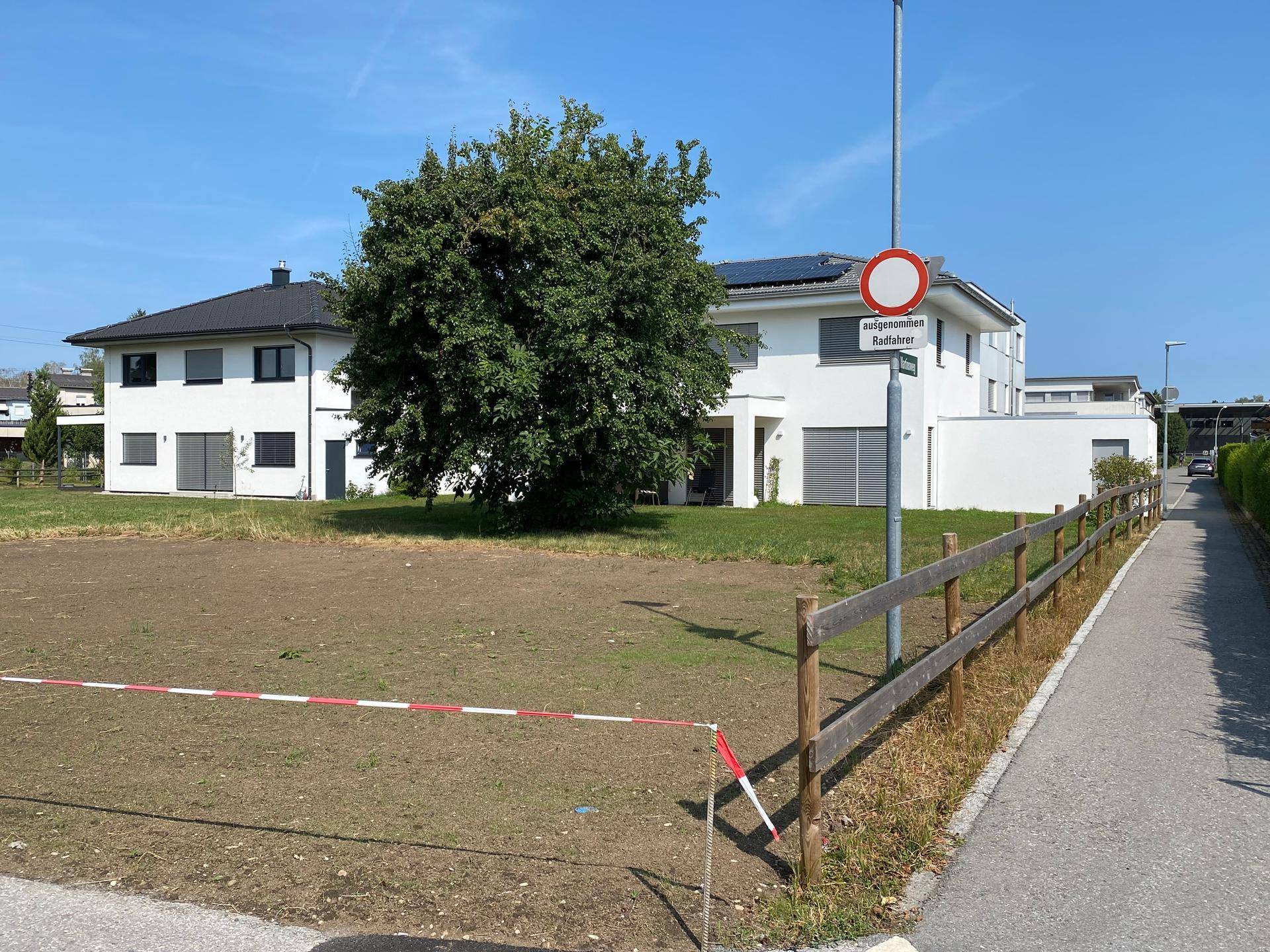 Unbebautes Grundstück mit angrenzendem Gehweg und Holzzaun, umgeben von modernen Wohnhäusern.