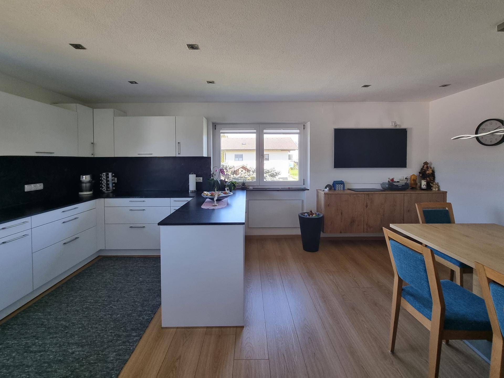 Moderne offene Küche mit Essbereich, weißen Schränken und Holzfußboden.