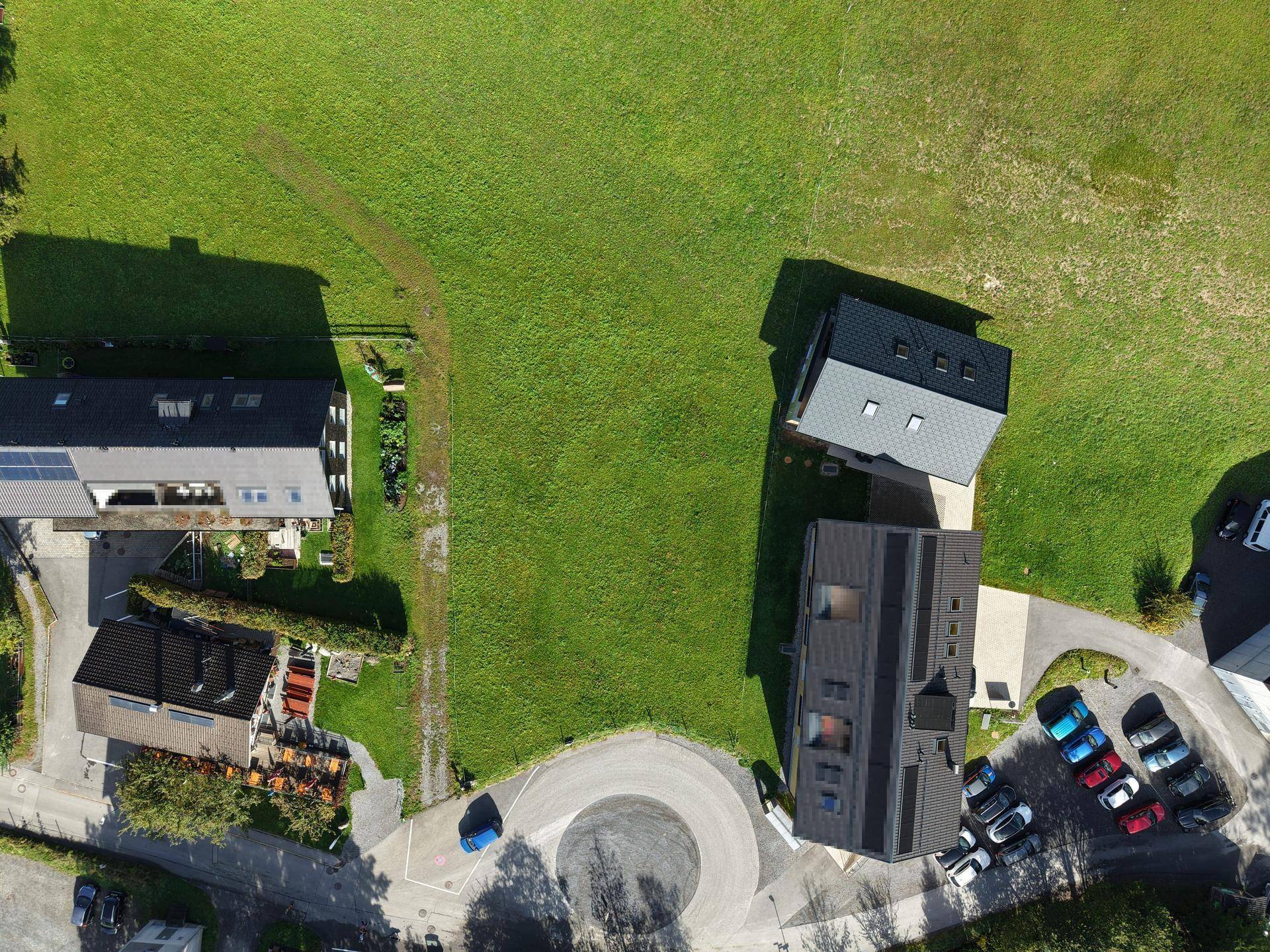 Vogelperspektive auf ein großes grünes Grundstück, umgeben von Wohnhäusern und einer kleinen Straße.