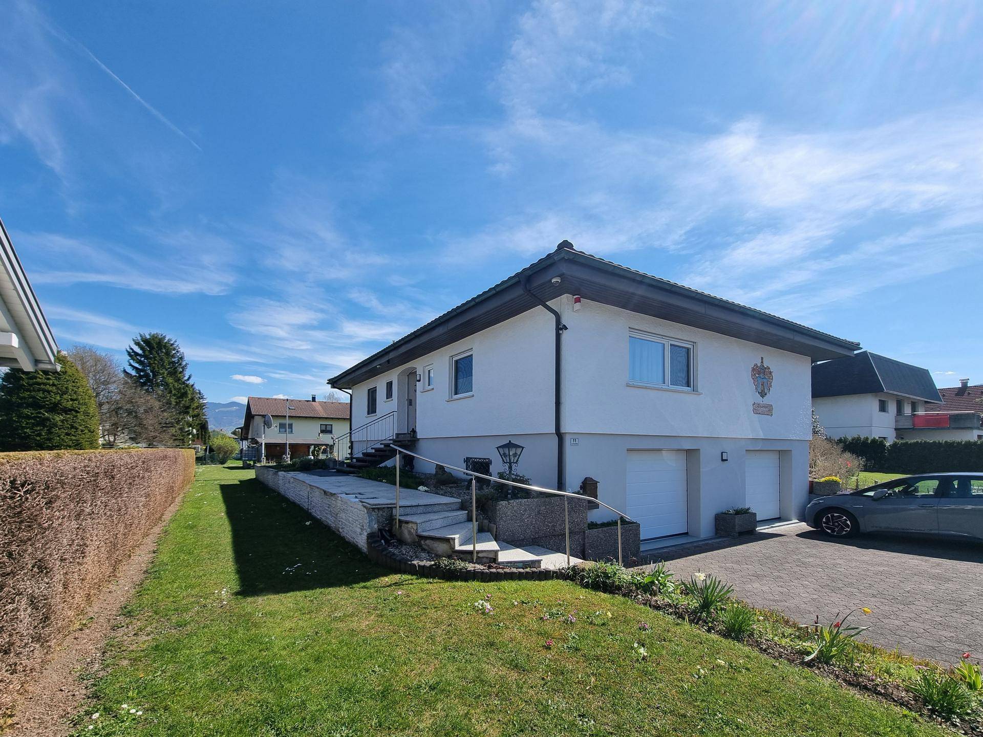 Das Haus von der Seite mit Treppenaufgang, Einfahrt und grüner Hecke.