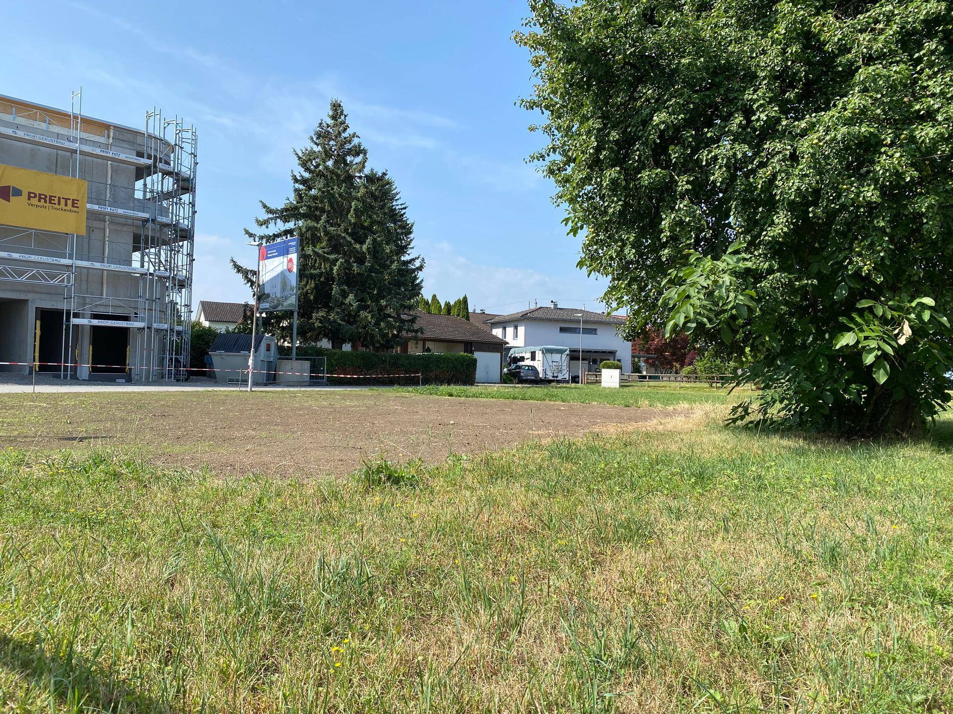 Grundstück mit vorbereiteter Fläche für Neubau und umliegenden Wohnhäusern unter blauem Himmel.