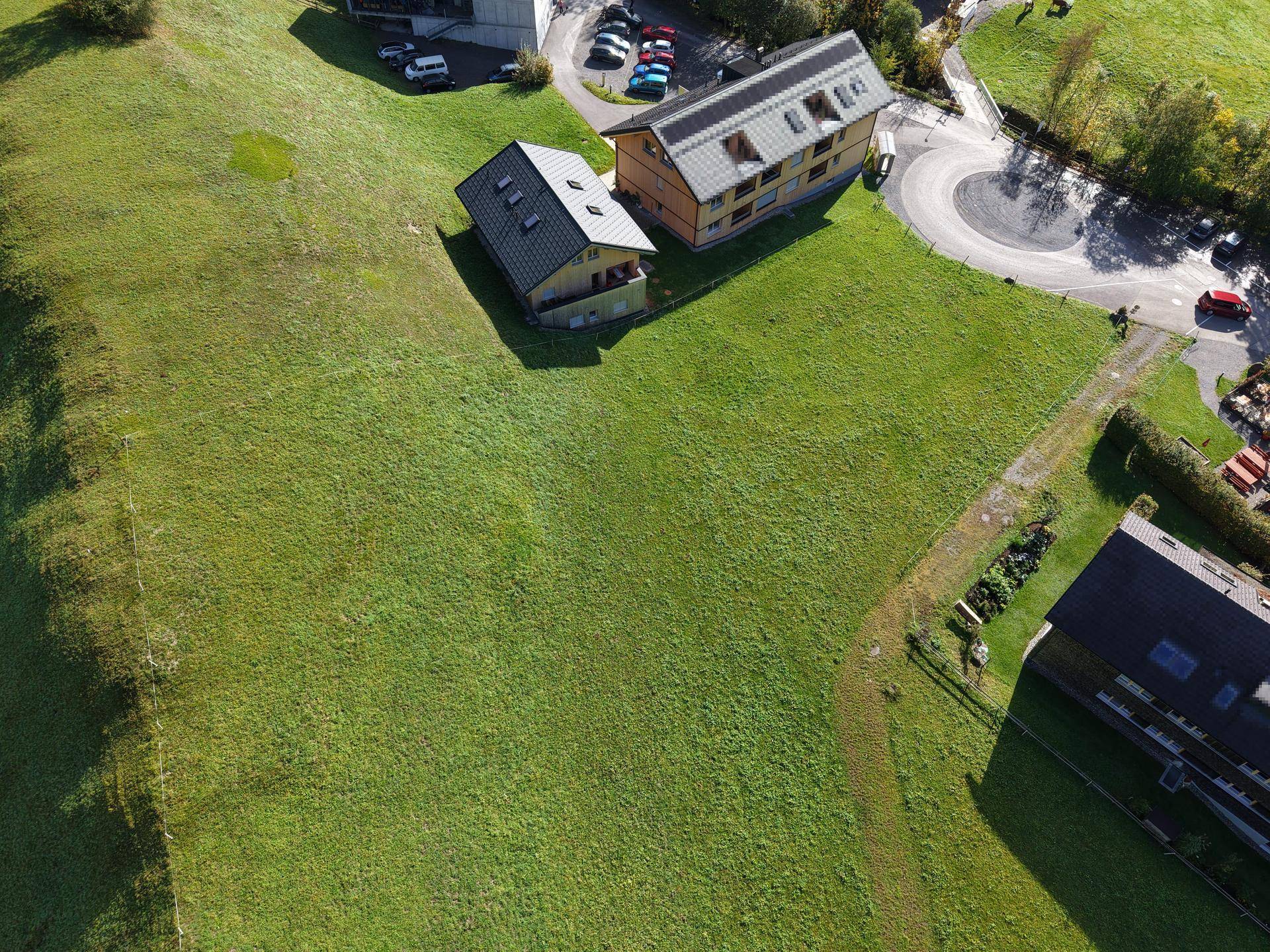 Luftaufnahme eines großen, grünen Grundstücks mit angrenzenden Häusern und einem Parkplatz.