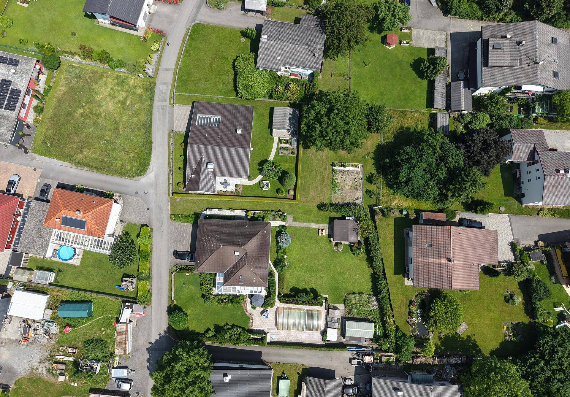 Luftaufnahme eines Wohngebiets mit Einfamilienhäusern, Gärten und Straßenverlauf.