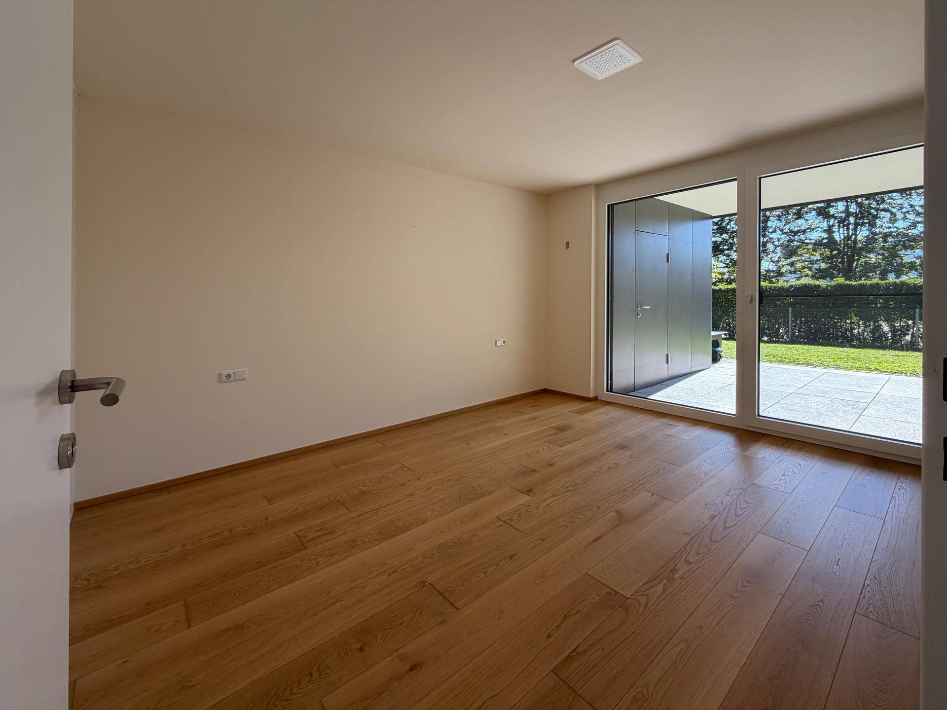 Helles Zimmer mit Holzfußboden und großen Fenstern mit direktem Zugang zur Terrasse.