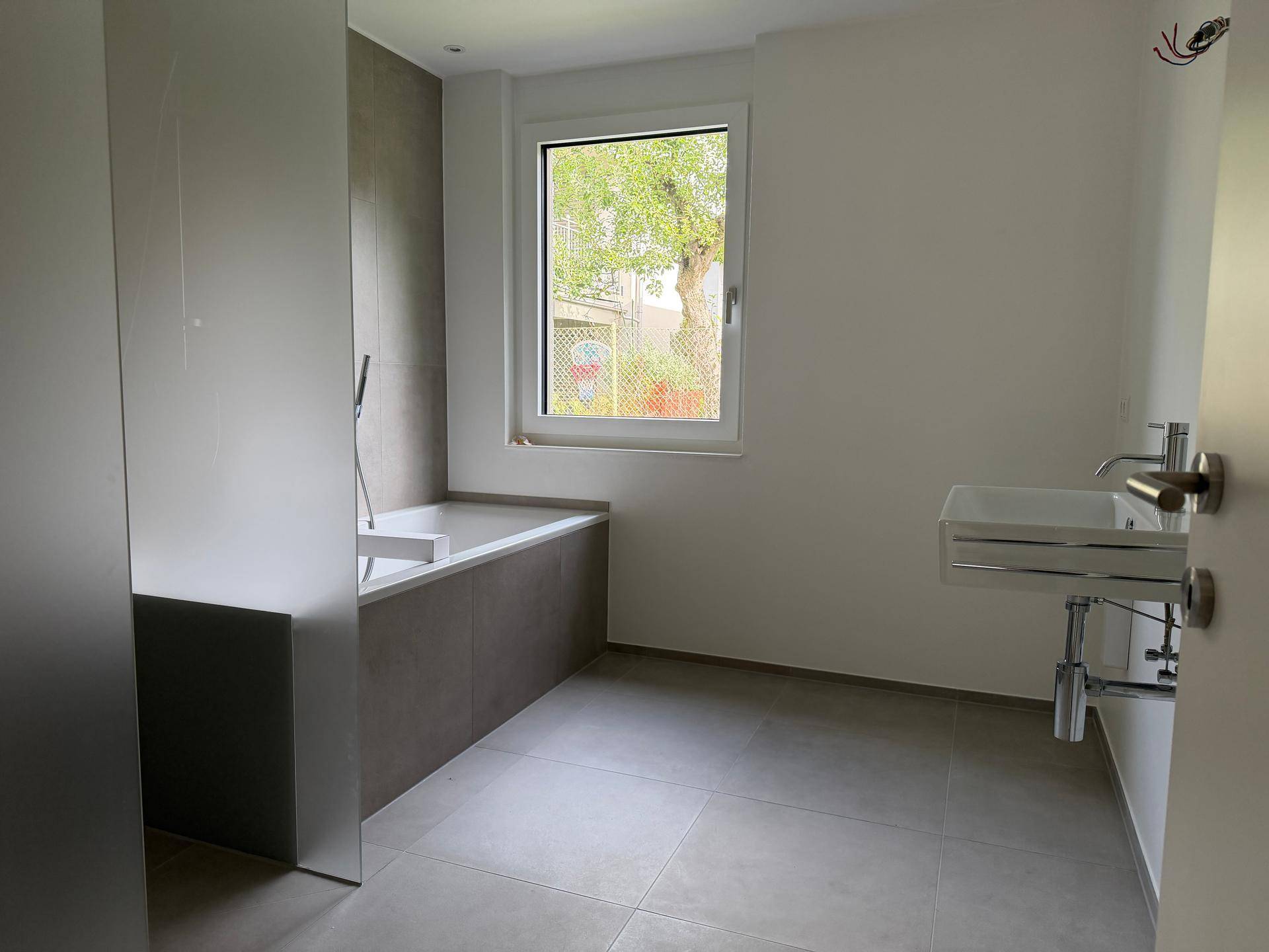 Unmöbliertes Badezimmer mit Badewanne, Waschbecken und Fenster, bereit zur Gestaltung.