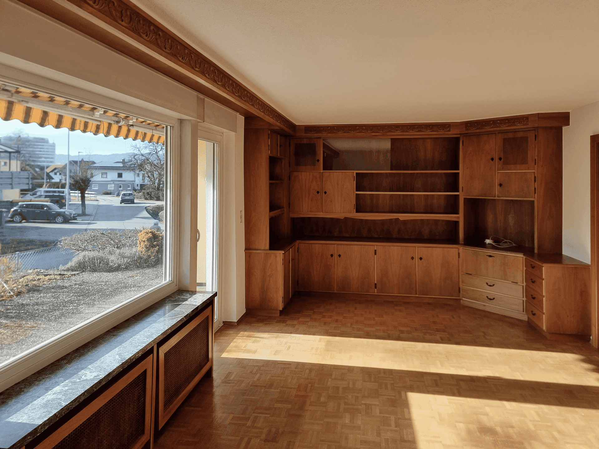 Helles Wohnzimmer mit Parkettboden und einer großen, maßgefertigten Holzschrankwand.