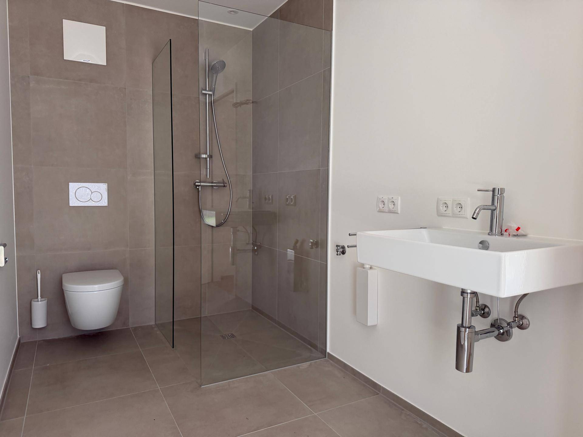 Modernes Badezimmer mit ebenerdiger Dusche, wandhängendem WC und Einzelwaschbecken.