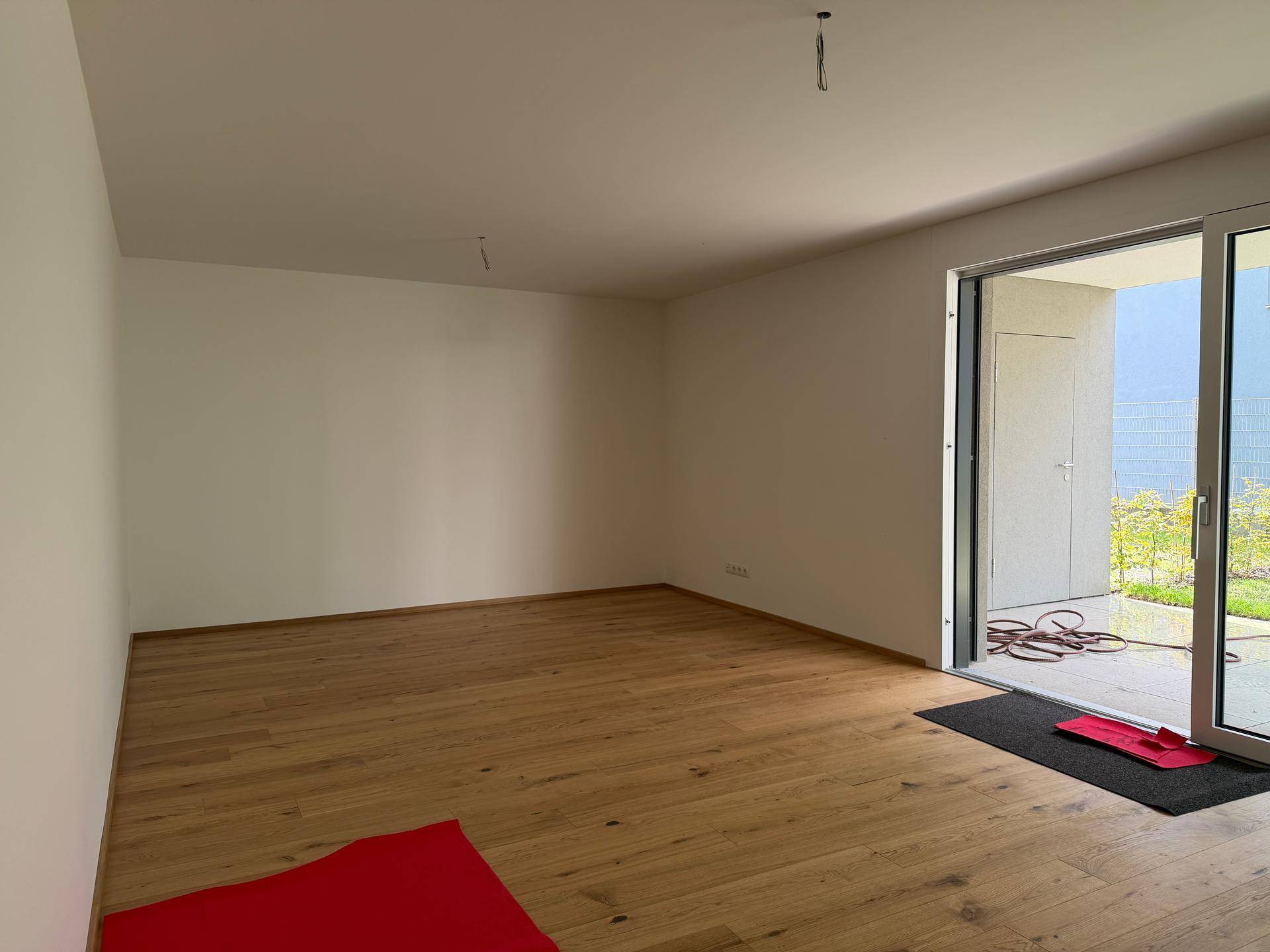 Leeres Zimmer mit hellem Holzfußboden und Zugang zu einem Außenbereich durch eine Schiebetür.