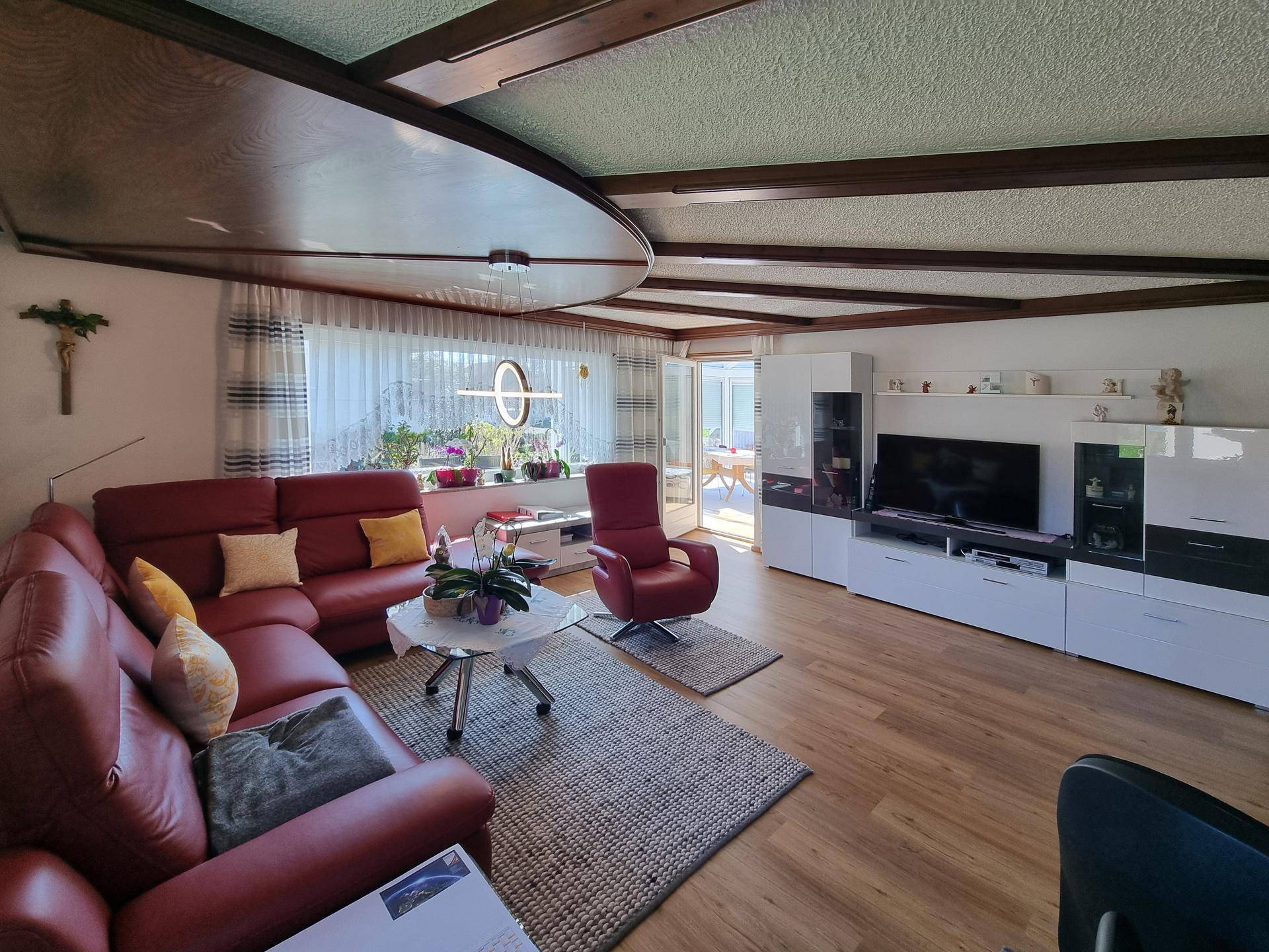 Geräumiges Wohnzimmer mit TV-Möbeln, Holzbalkendecke und Zugang zum Wintergarten.