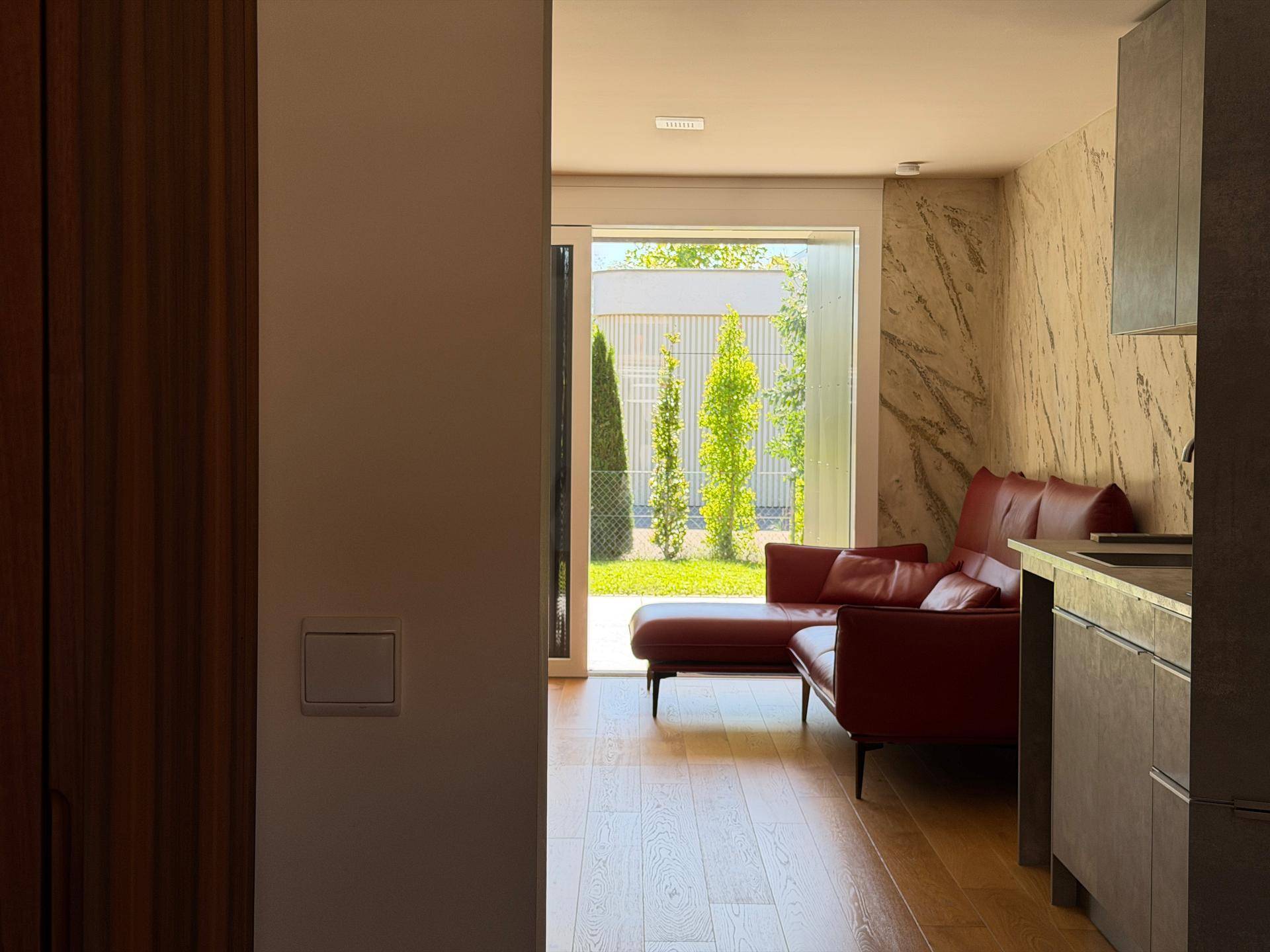 Blick vom Flur in den Wohnbereich mit rotem Sofa und Zugang zur Terrasse durch große Fenster.