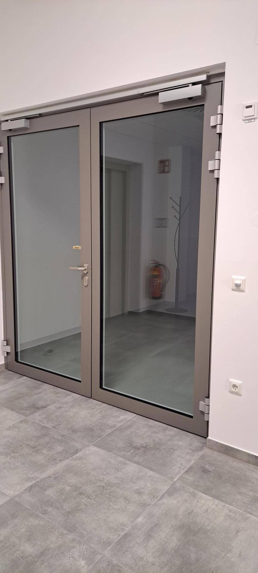 Moderner Flur mit grauen Fliesen und großen Glastüren, die in einen weiteren Bereich führen.