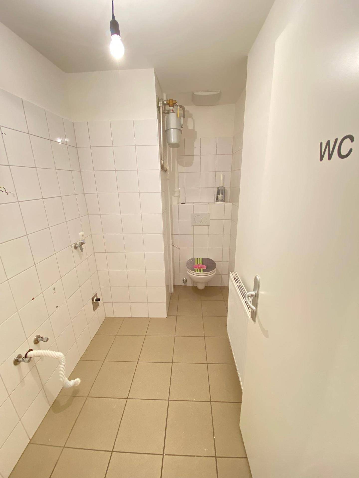 Einfache Gästetoilette mit Fliesenboden und weiß gefliesten Wänden, die funktional und sauber ist.
