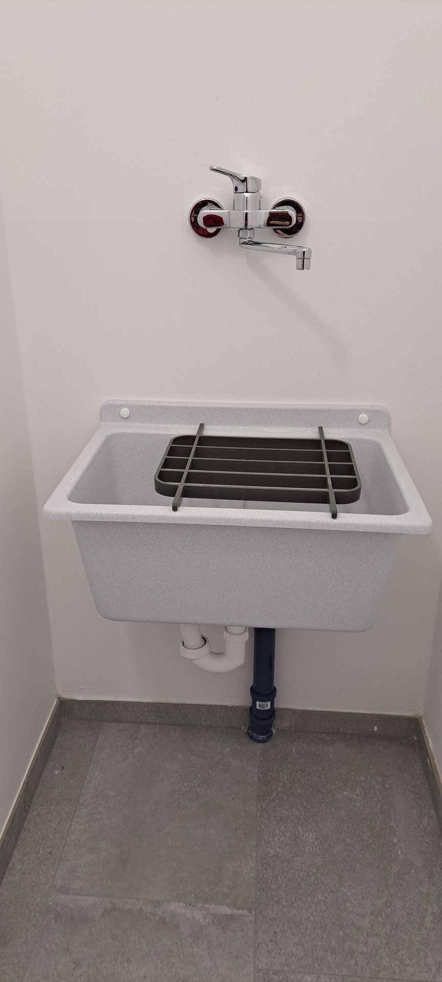Einfaches Waschbecken mit Gitterrost in einem funktionalen Raum, ideal für Reinigungsarbeiten.