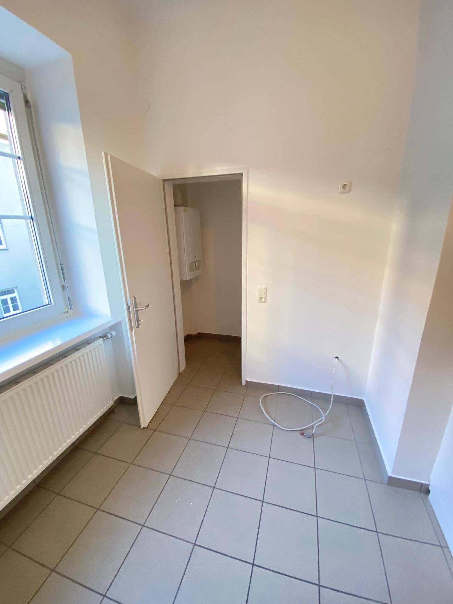 Kleiner Raum mit Fliesenboden und einem Fenster, der als Hauswirtschaftsraum oder Abstellraum dienen könnte.