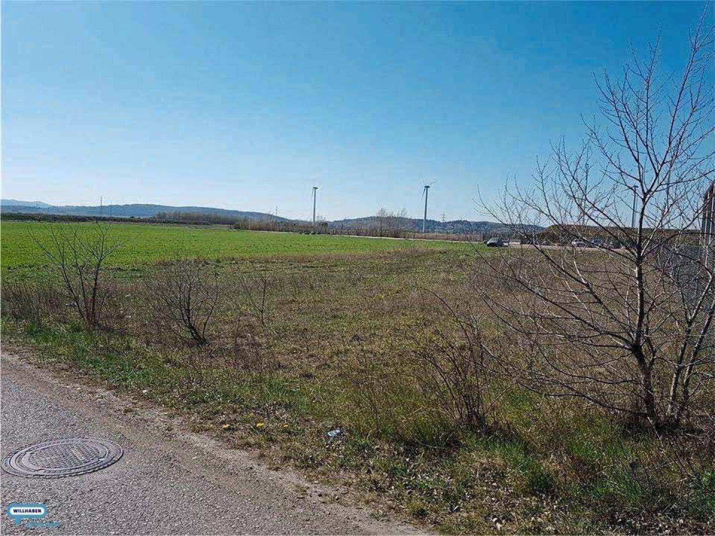 Offenes Feld mit unbefestigtem Weg und Blick auf die hügelige Landschaft in der Ferne.