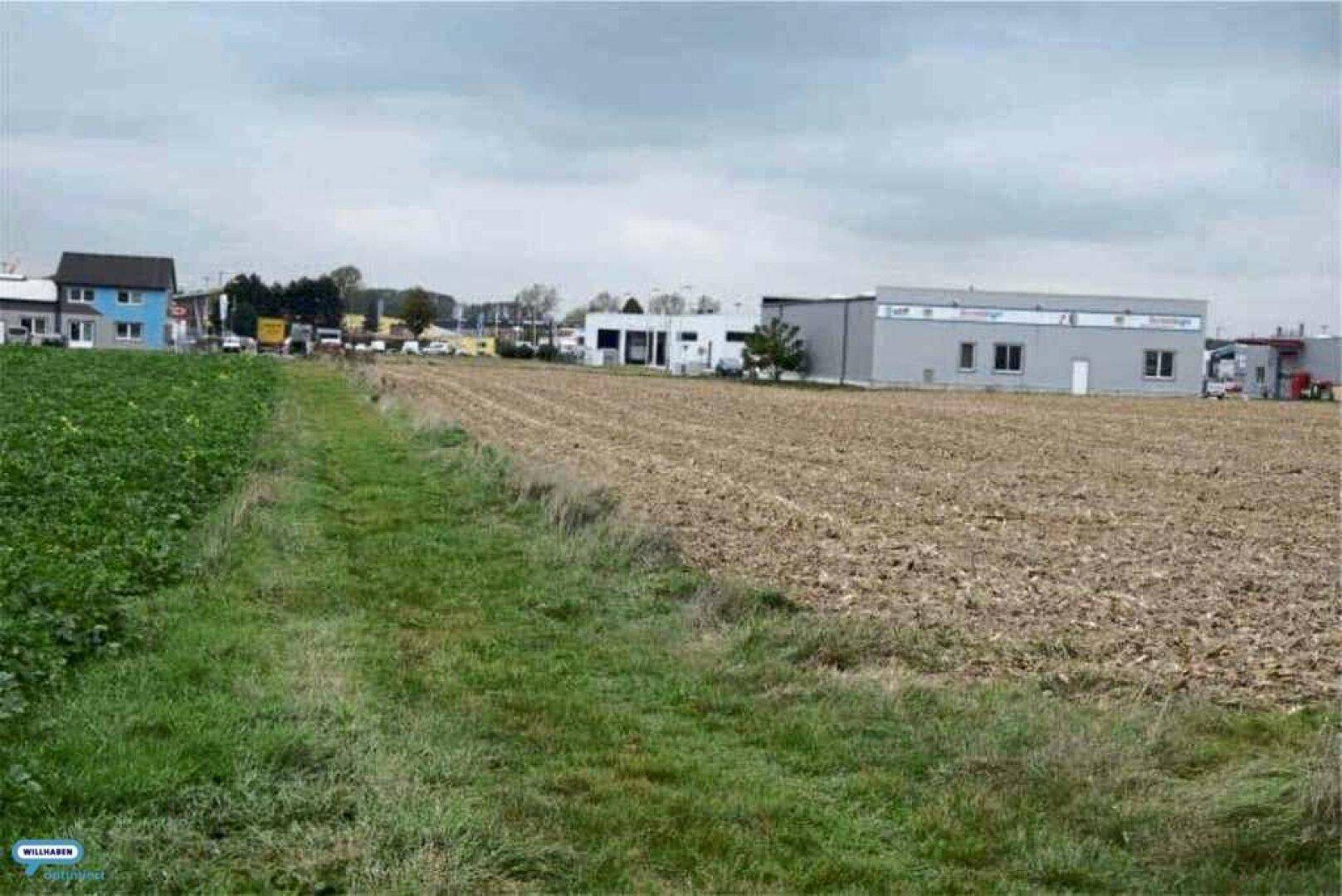 Weitläufiges Feld mit angrenzenden Gewerbegebäuden und einer Straße in der Ferne.