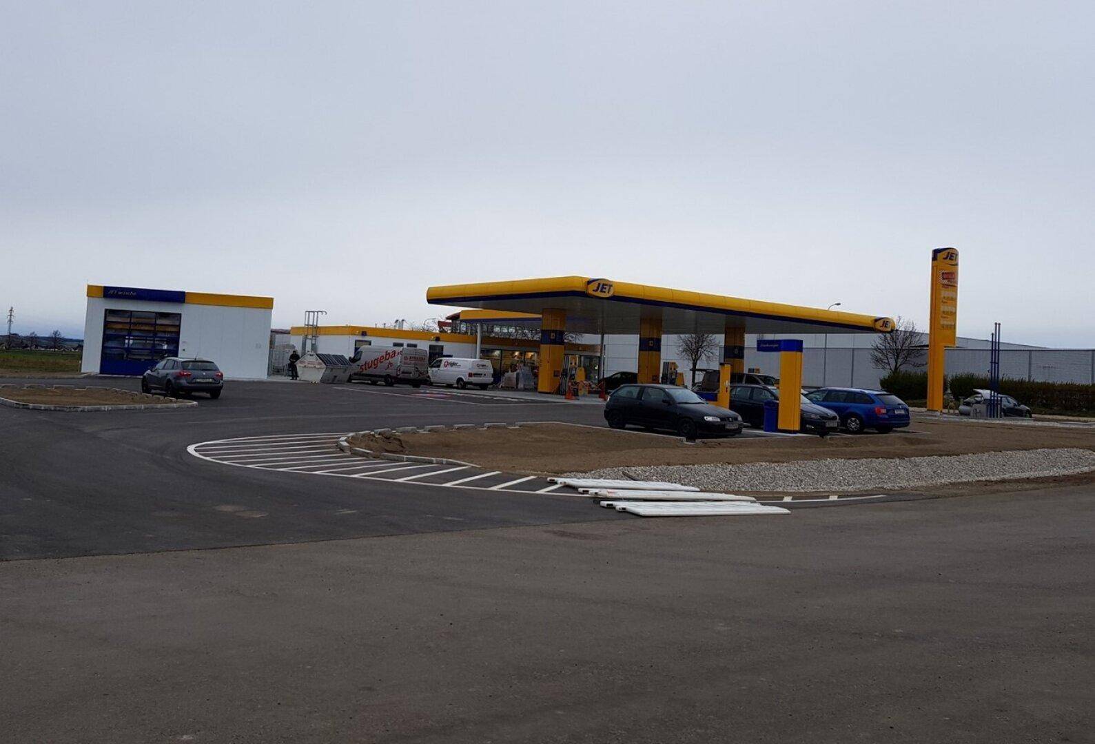 Weitläufige Ansicht einer modernen JET-Tankstelle mit mehreren Zapfsäulen und einer Autowaschanlage unter Wolken.