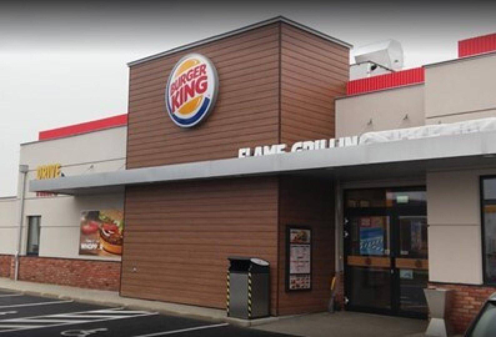 Eingangsbereich eines Burger King Restaurants mit markantem Logo und Holzverkleidung an der modernen Fassade.