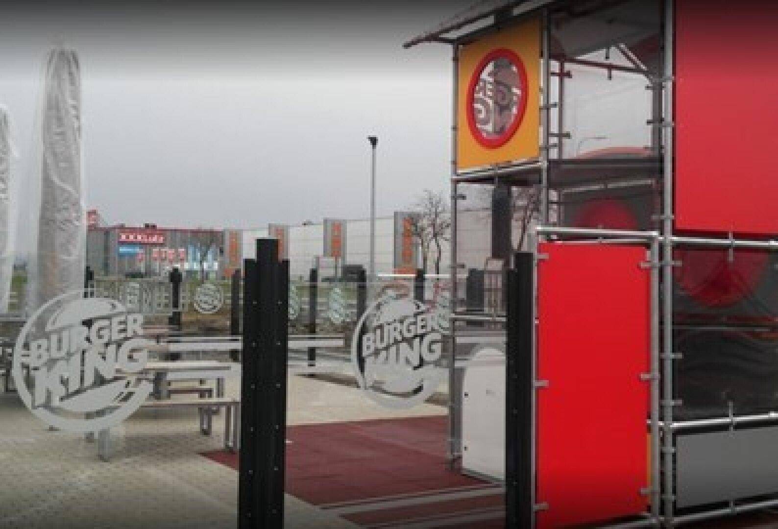 Außenbereich eines Burger King Restaurants mit Tischen und Stühlen, umgeben von roten und transparenten Paneelen.