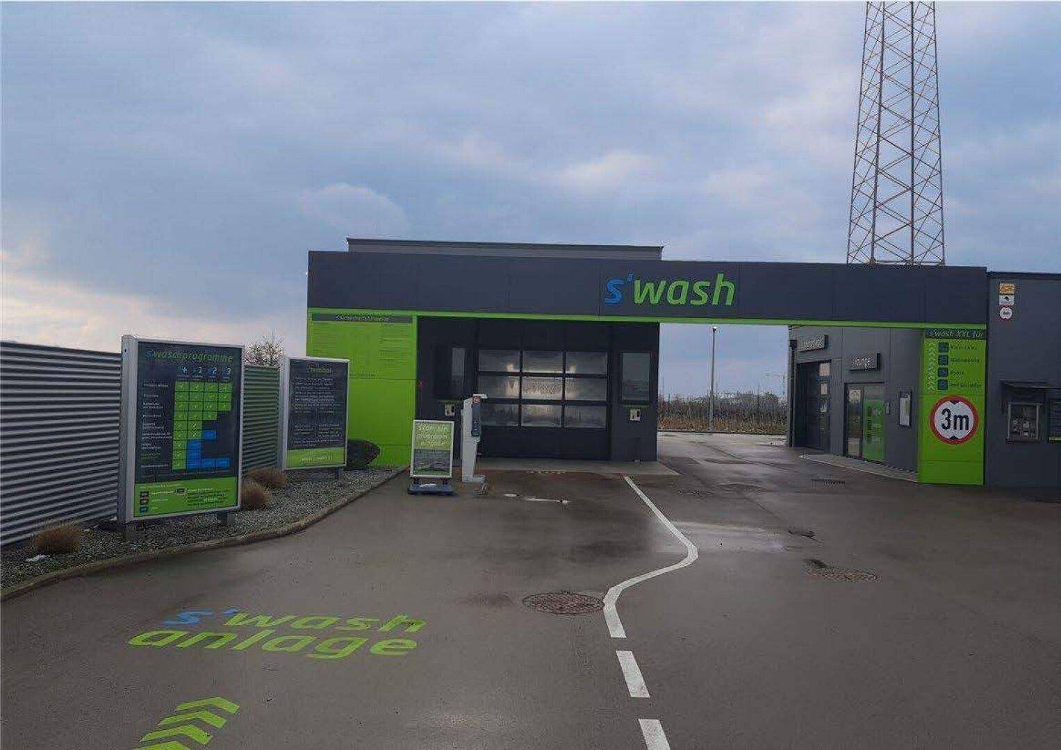Eingangsbereich der Autowaschanlage an einem bewölkten Tag mit Hinweisschildern und Fahrbahnmarkierungen.