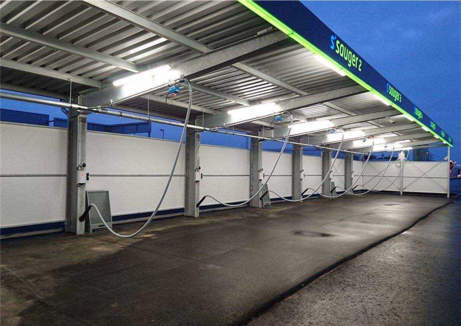 Überdachte Staubsaugerplätze der Autowaschanlage bei Dämmerung mit Beleuchtung und Schläuchen.