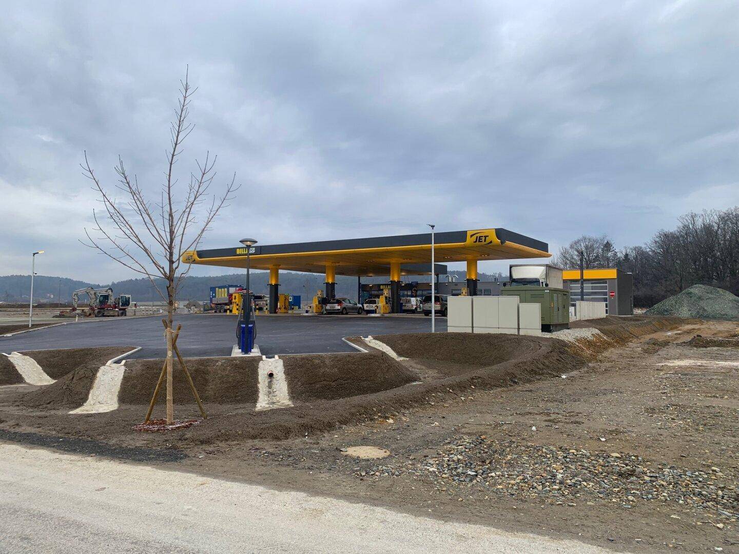 Moderne Tankstelle mit gelb-schwarzem Dach und Baustellenbereich im Vordergrund unter bewölktem Himmel.