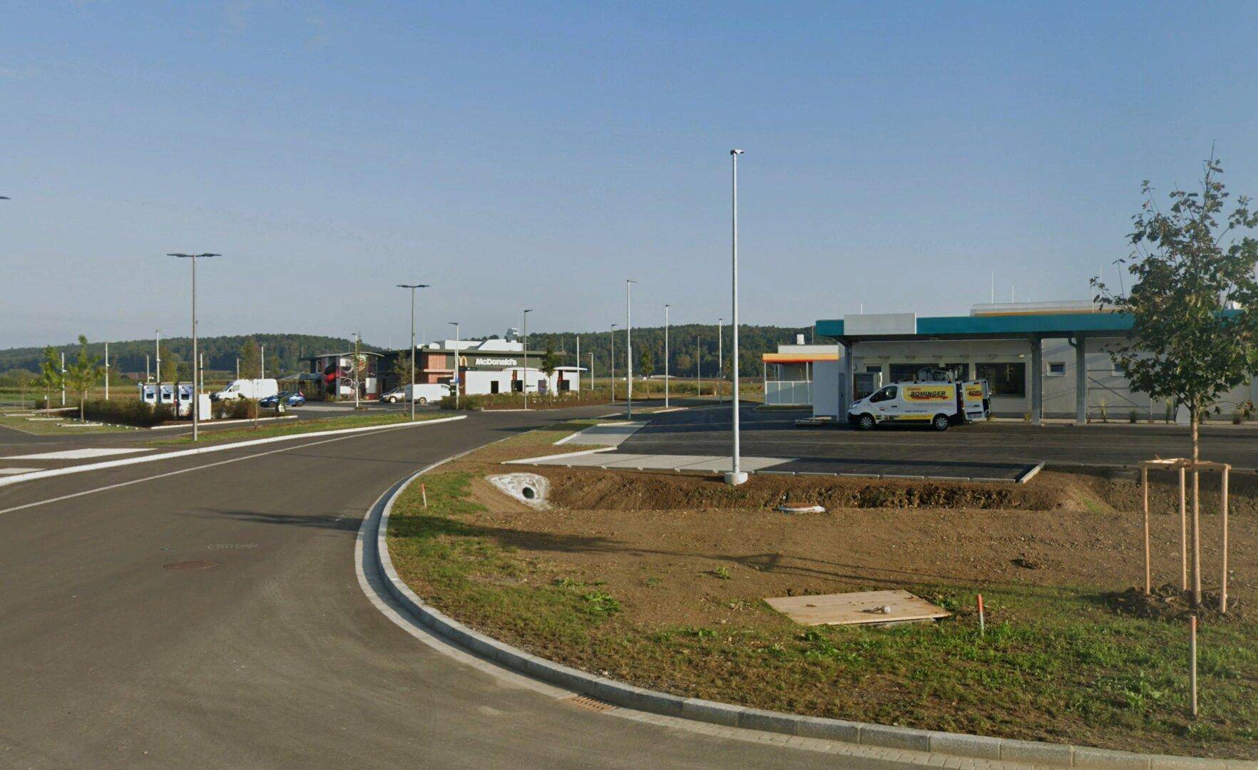 Gewerbegebiet mit Tankstelle und Fast-Food-Restaurant unter klarem blauem Himmel und weitläufigen Parkflächen.