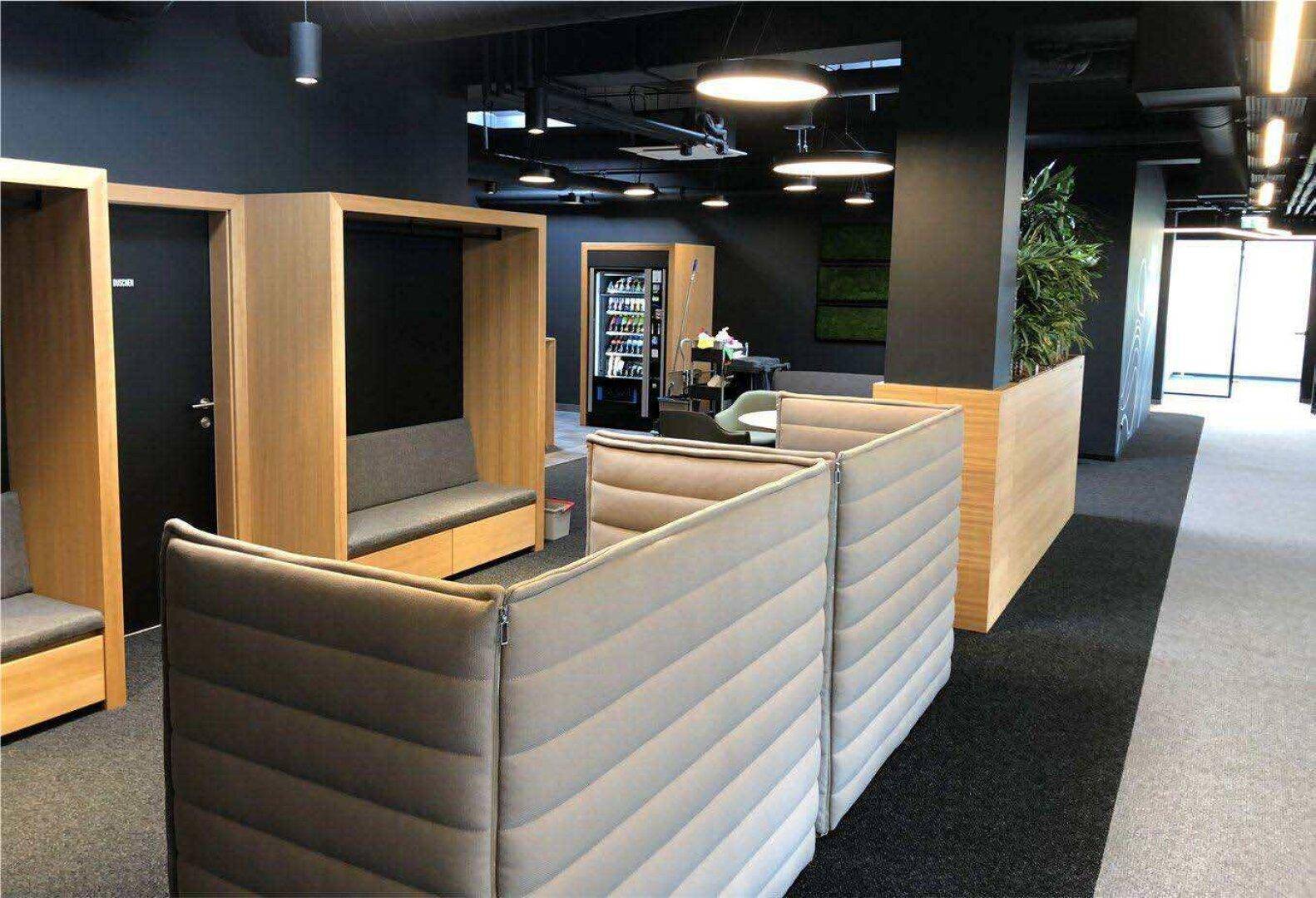Moderner Bürobereich mit schallgedämmten Arbeitskabinen, dunklem Teppichboden und Holzelementen.