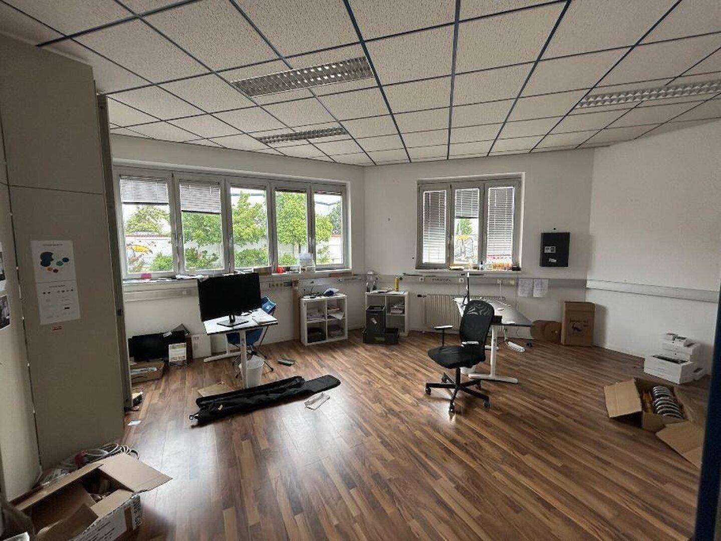 Helles Büro mit Laminatboden, großen Fenstern und Jalousien, ausgestattet mit Büromöbeln.