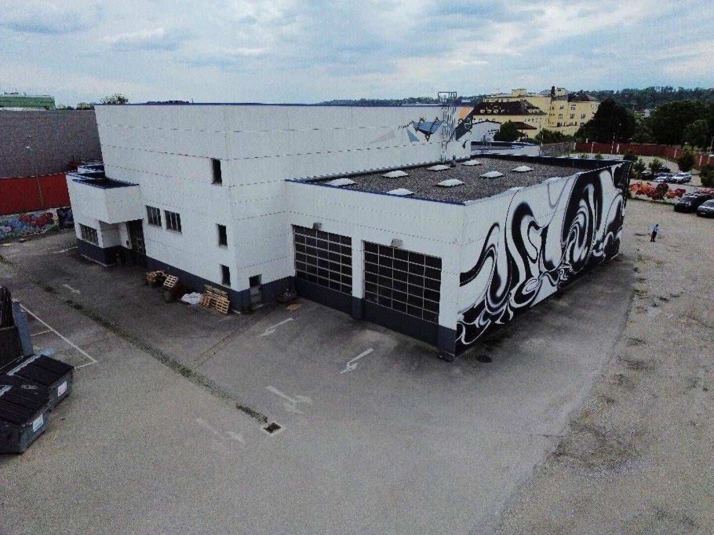 Seitenansicht des Gewerbegebäudes mit großen Rolltoren und künstlerischen Graffiti-Elementen an der Fassade.