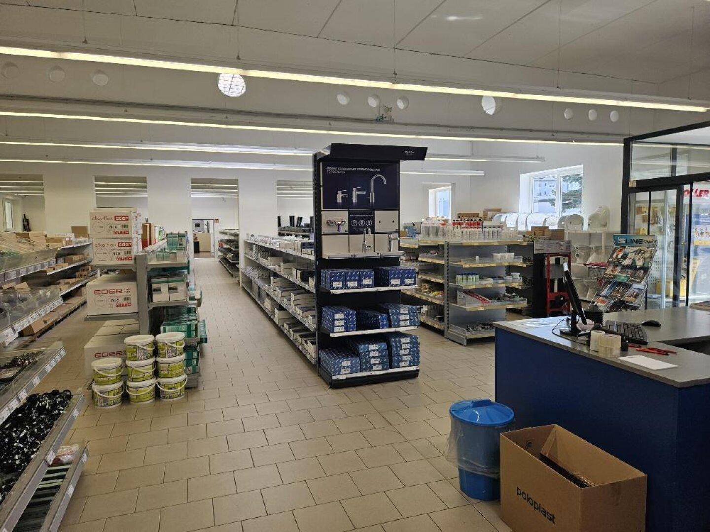 Heller Verkaufsraum mit Regalen voller Produkte und einem Kassenbereich im Vordergrund.