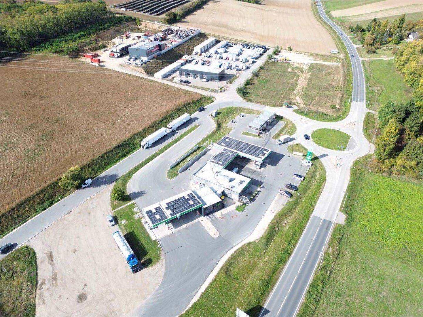 Detaillierte Luftaufnahme der Tankstelle mit Kreisverkehr, umgeben von landwirtschaftlichen Flächen und Gewerbebauten.