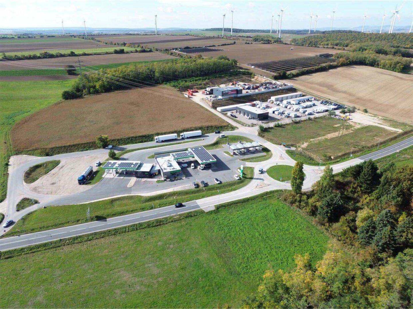 Panoramablick aus der Luft auf das Gewerbegebiet, umgeben von Feldern und Windkraftanlagen am Horizont.