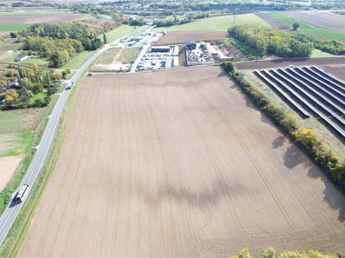 Weitläufige Luftaufnahme der landwirtschaftlichen Flächen mit dem Gewerbegebiet und Solaranlagen im Hintergrund.