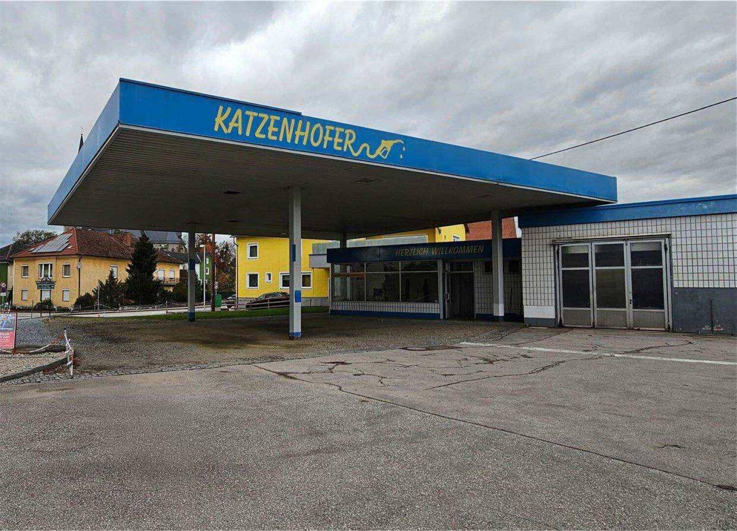 Vorderansicht der ehemaligen Tankstelle Katzenhofer mit markanter blauer Überdachung und dem Schriftzug 'Herzlich Willkommen'.