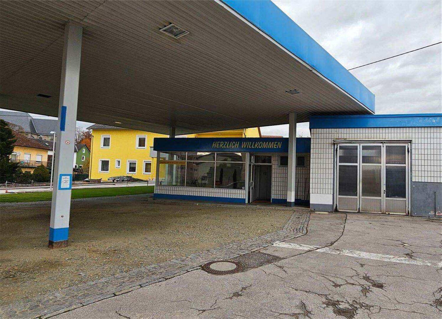 Detaillierte Ansicht des Eingangs und der Servicebereiche der ehemaligen Tankstelle unter der blauen Überdachung.