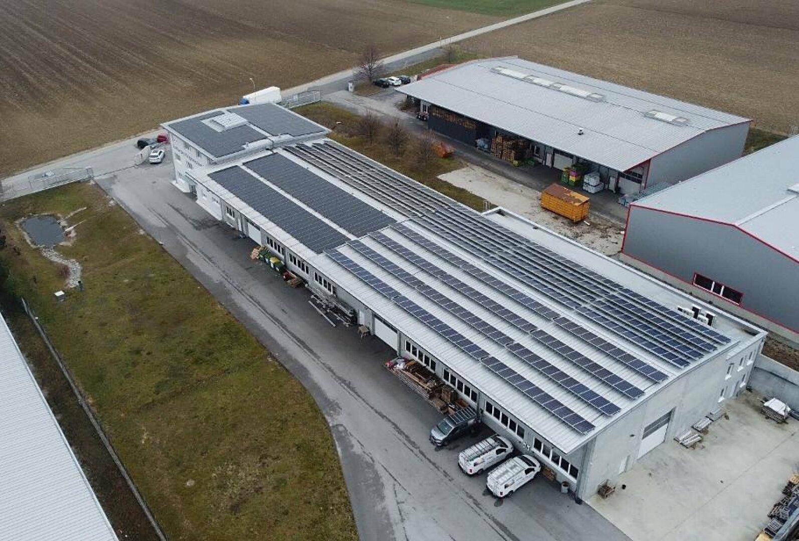 Weitläufige Luftaufnahme eines Gewerbekomplexes mit umfangreicher Photovoltaikanlage und angrenzenden Feldern.