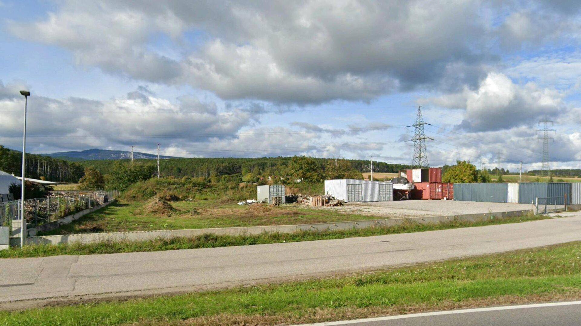 Weitläufiges Außengelände mit Lagercontainern und Blick auf bewaldete Hügel unter bewölktem Himmel.