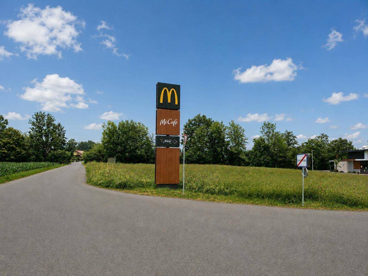 Großes McDonald's-Schild vor einer weiten Grünfläche unter blauem Himmel.