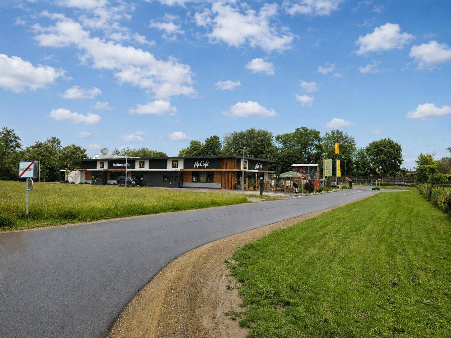McDonald's Restaurantgebäude mit Drive-in-Bereich, umgeben von Grünflächen und Zufahrtsstraße.