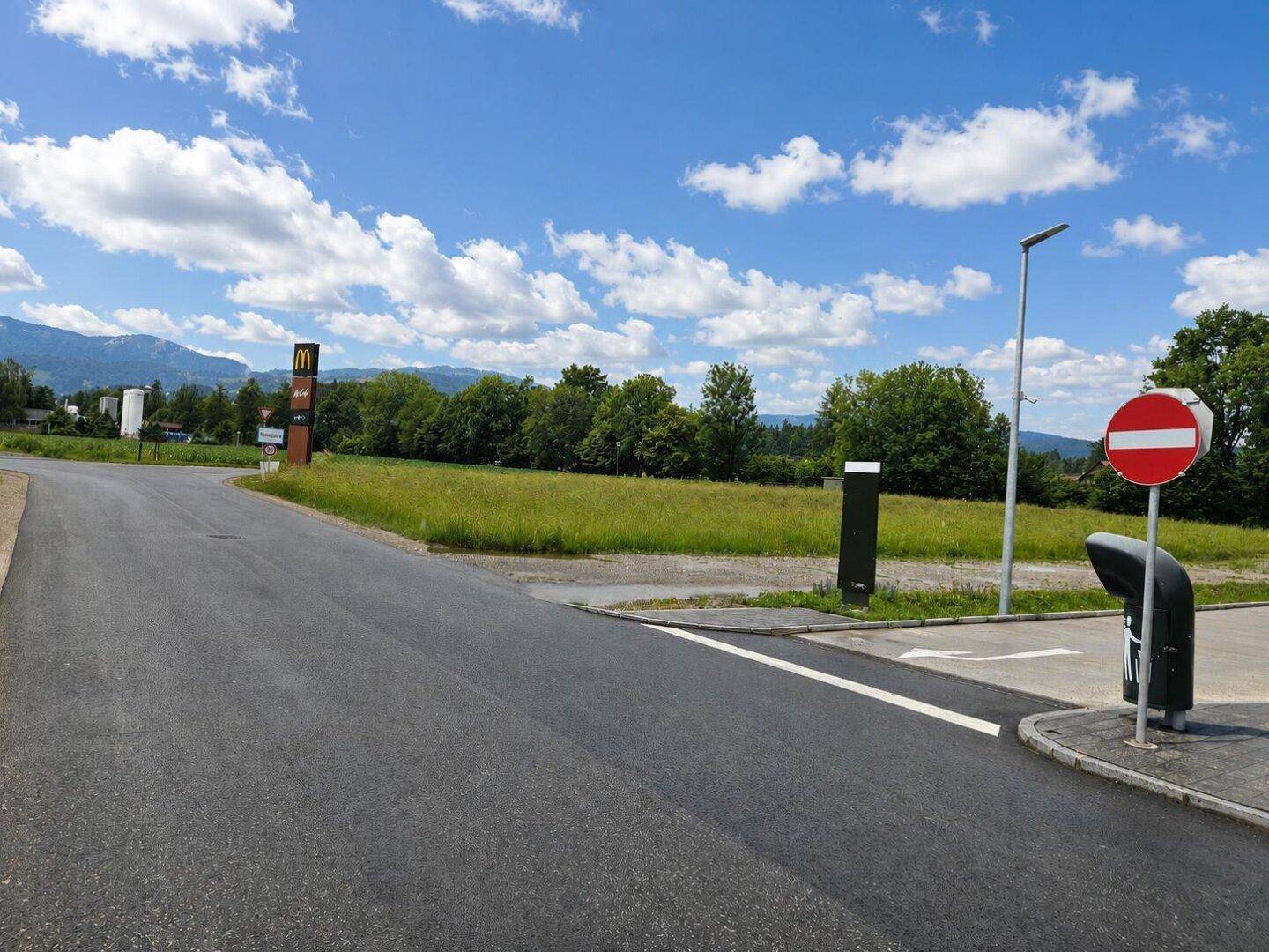 Zufahrtsstraße zu einem unbebauten Grundstück mit McDonald's-Schild im Hintergrund.