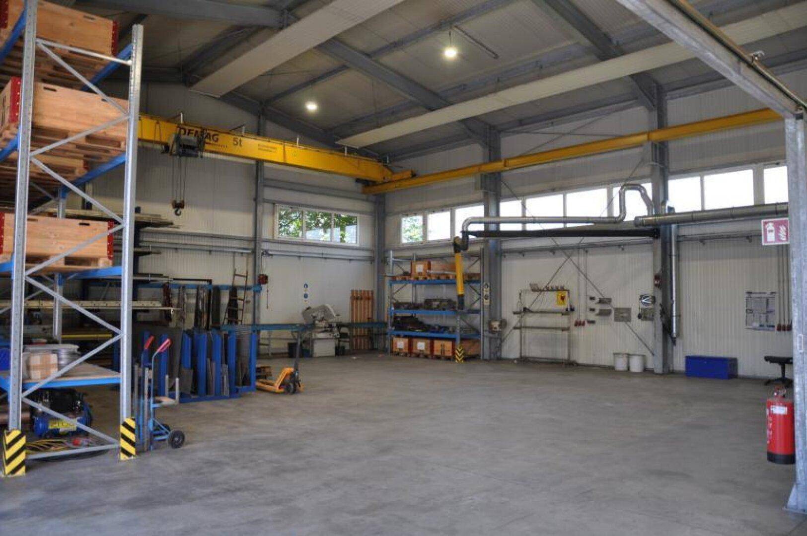 Industrielle Lagerhalle mit Regalen, Krananlage und großen Fenstern für Tageslicht.